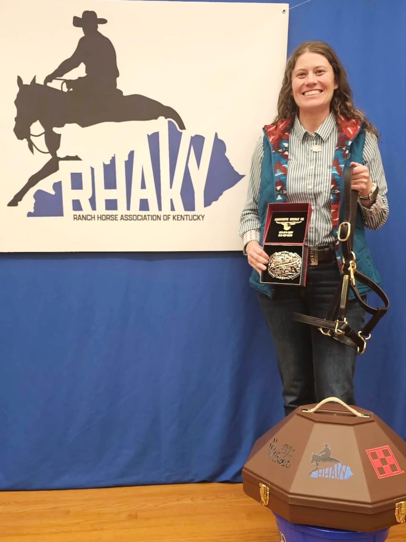 A rider holding a buckle and award beside show tack after a ranch-horse event