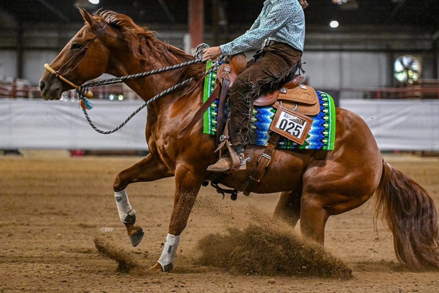 A horse and rider performing a reining stop in an indoor arena