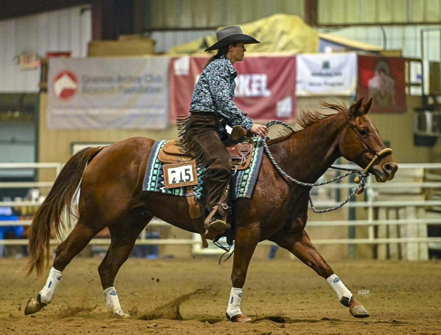 A horse and rider moving through a reining pattern in a show arena