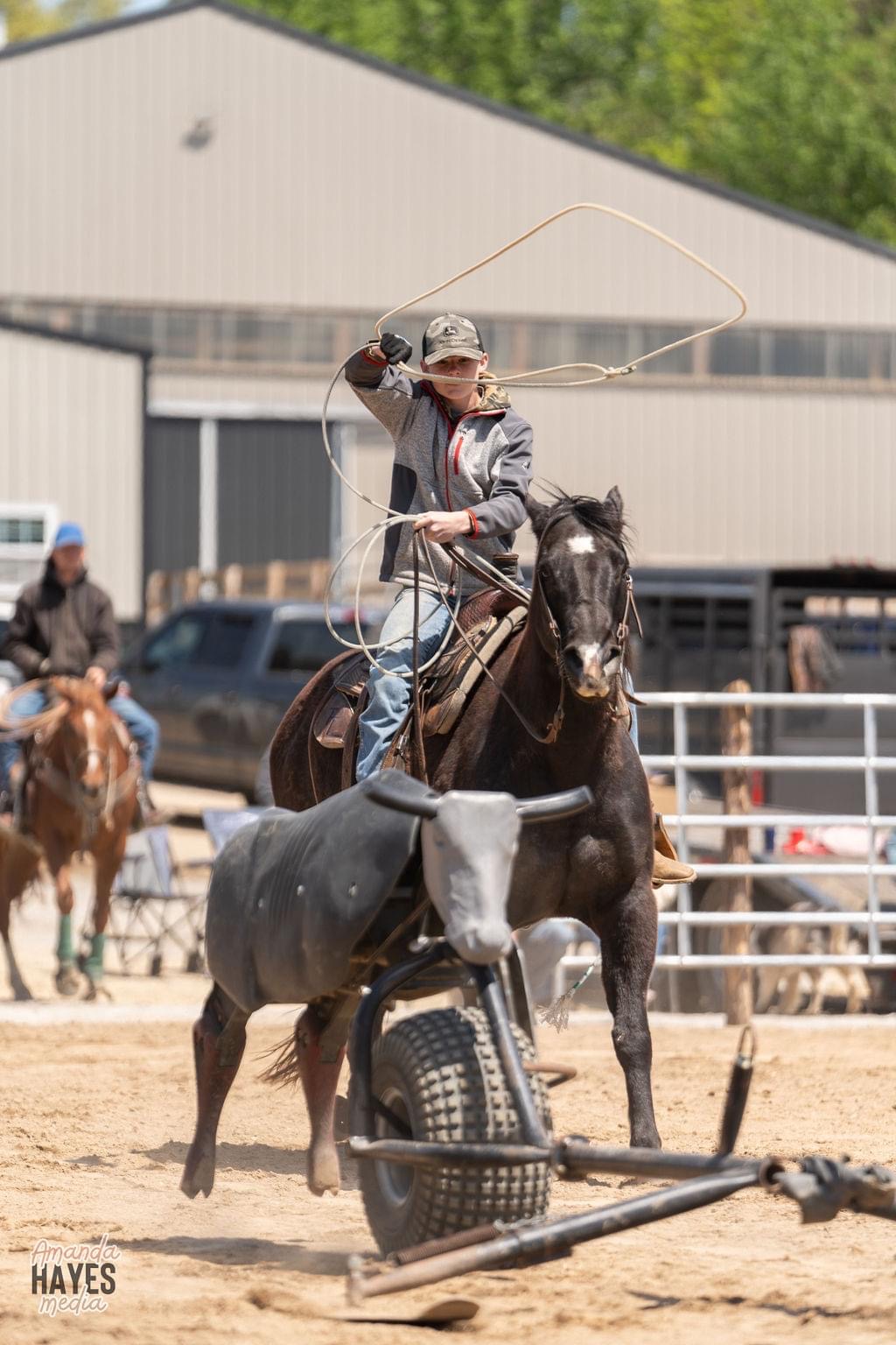 A rider practicing a controlled rope swing from horseback in a ranch arena