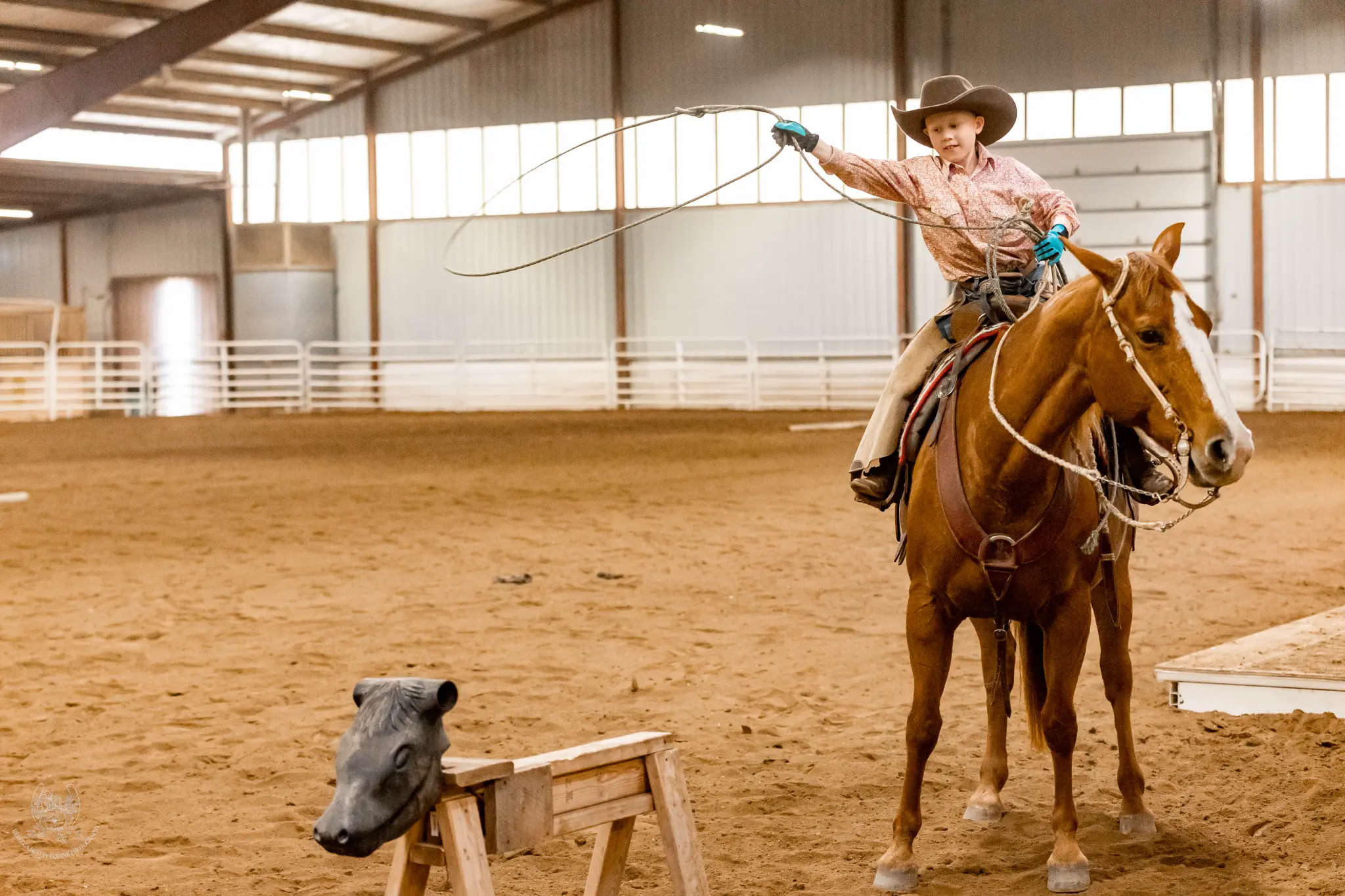 A young rider practicing roping from horseback with a roping dummy in an indoor arena